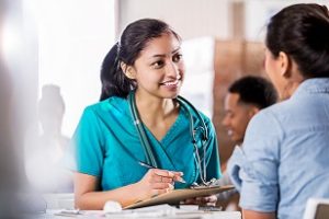 Young female Hispanic volunteer healthcare professional talks with female patient about her medical history.